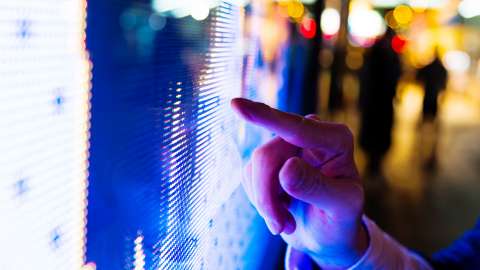 El dedo de un hombre señala la pantalla LED del precio del mercado de valores por la noche